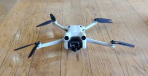 床の上に置かれた、折りたたみ式アームとカメラを備えた白い小型ドローン