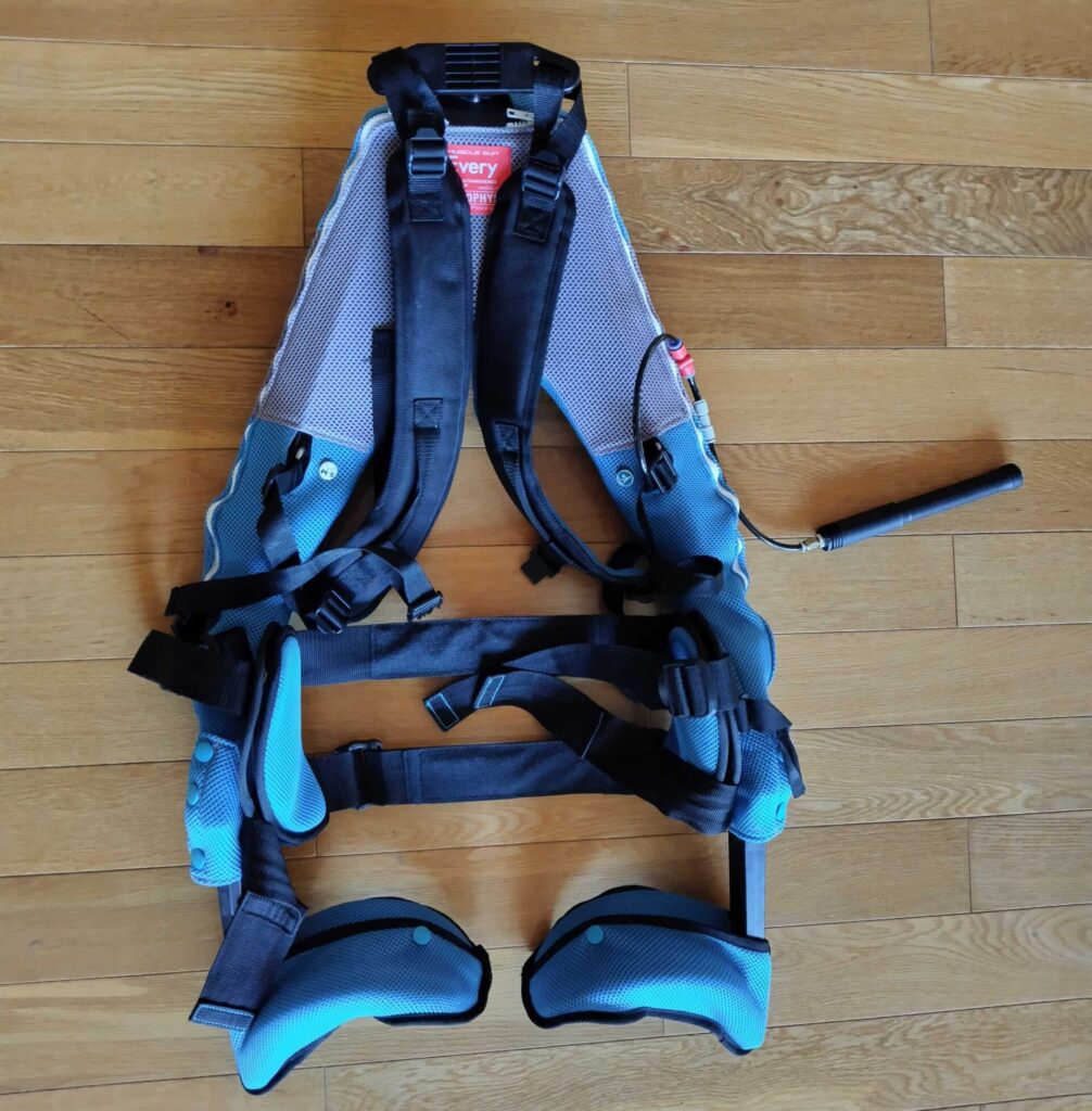 空気圧式のアシストスーツが床に置かれている。ポンプで空気を注入することで内部のエアバッグが膨らみ、腰や太ももへの負担を軽減する仕組みになっている。