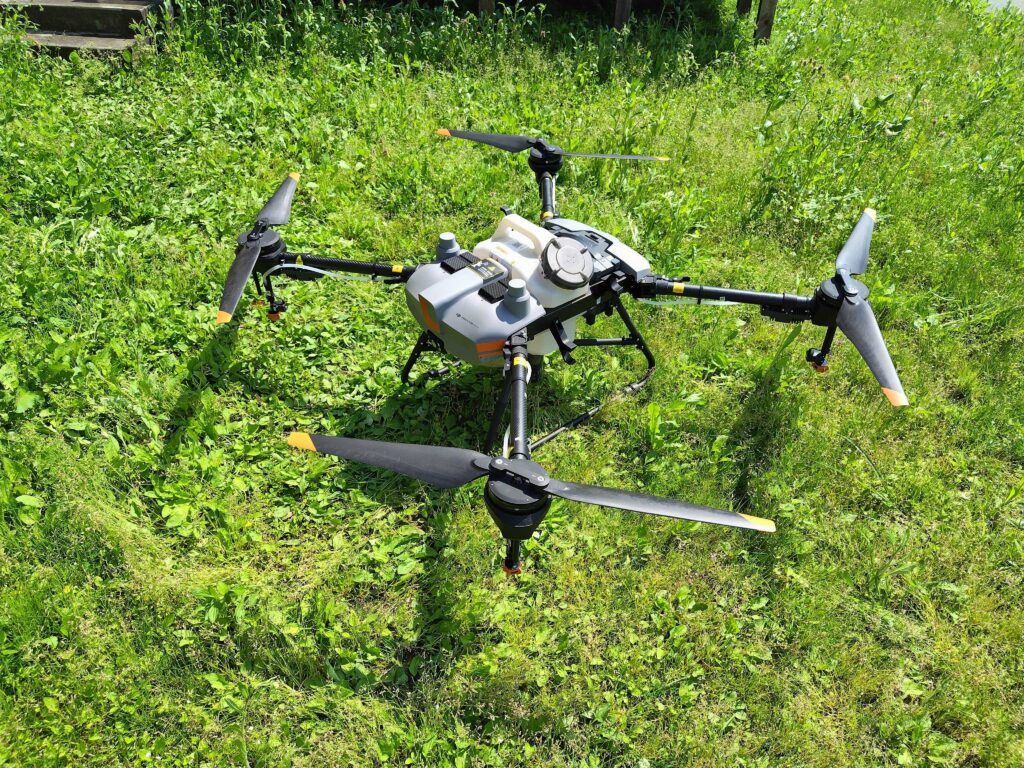 草地に設置された農業用ドローン。4枚のプロペラ、液剤タンク、ノズルなどを搭載し、農薬や肥料の自動散布に対応している。